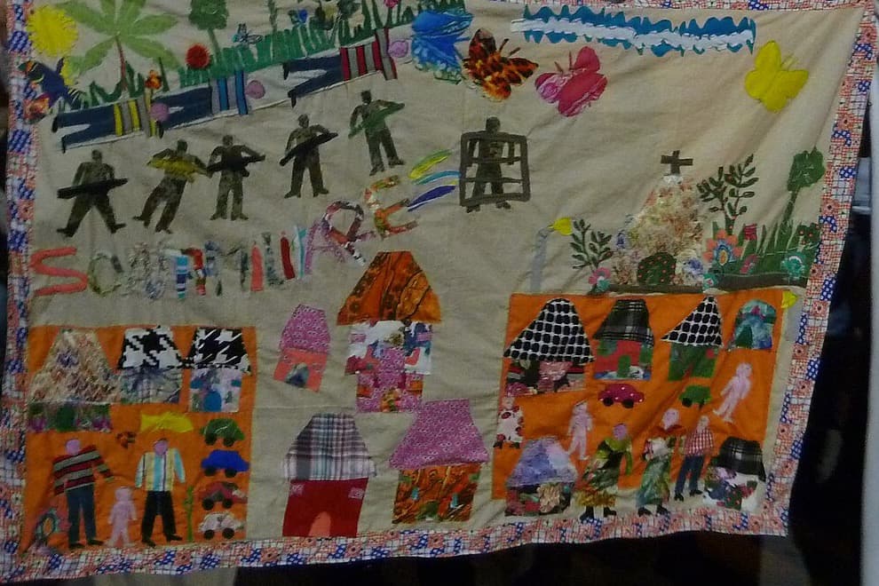 Colcha de retazos con casas, soldados, mariposas y palmeras, cosida en tela.