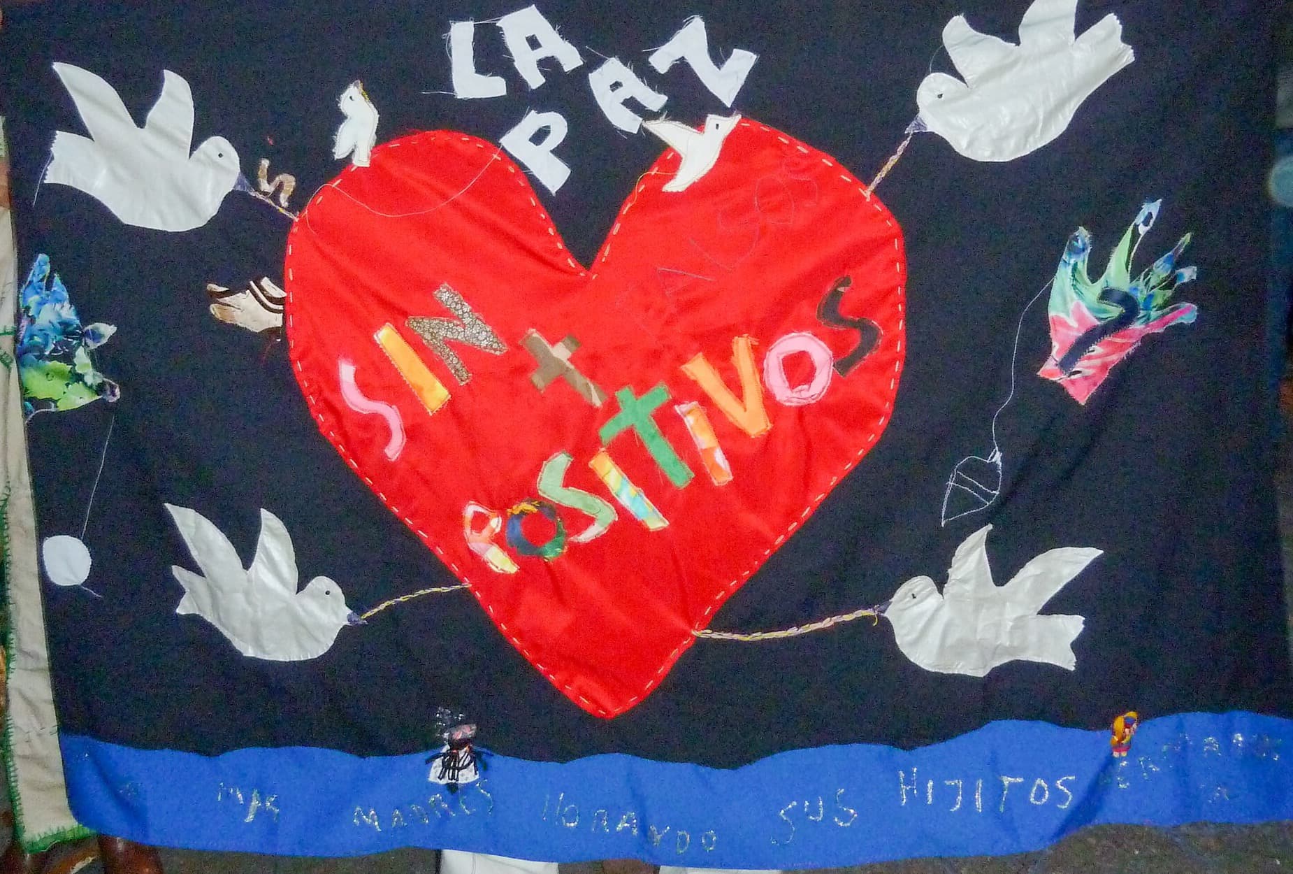 Tela bordada con un corazón rojo, palomas blancas y la frase «la paz sin positivos».