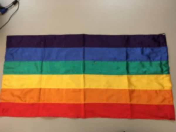 Bandera de seis franjas (violeta, azul, verde, amarillo, naranja y rojo) tendida sobre una mesa.